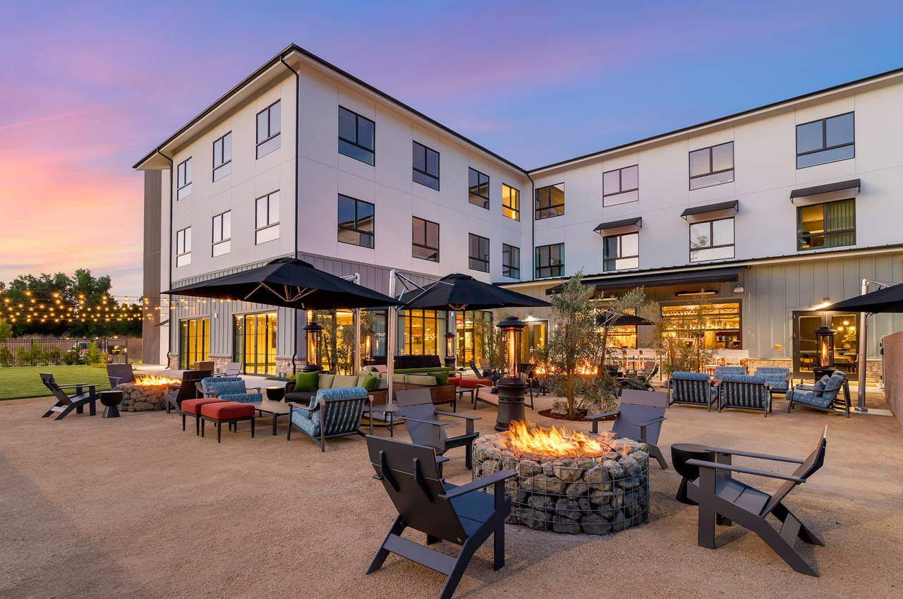 Hotel courtyard at sunset with fire pits, lounge chairs, and string lights creating a cozy outdoor space.